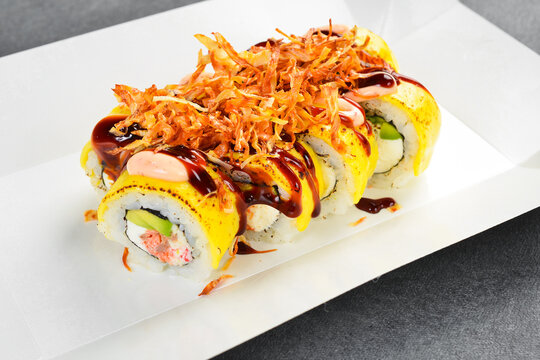 Gourmet sushi roll topped with melted cheddar cheese and crispy fried onion isolated on white background. Delicious Japanese rolls filled with cream cheese. Fresh meal.
