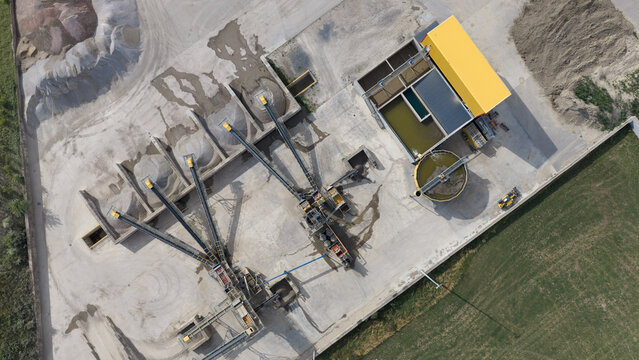Aerial view of a gravel and sand processing plant with conveyor belts, storage piles, and industrial machinery in an open industrial site in La Longueville, Hauts-de-France, France.