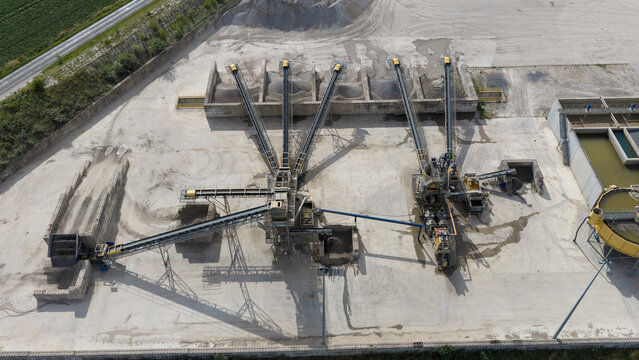 Aerial view of an industrial gravel processing plant with conveyor belts, piles of aggregate, and water treatment tanks in La Longueville, Hauts-de-France, France.