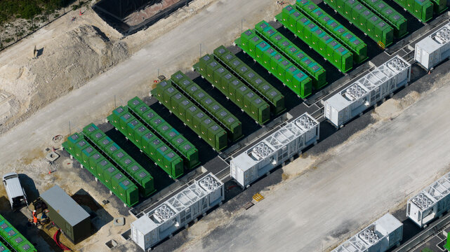 Aerial view of a battery energy storage system facility featuring rows of green battery containers and white power conversion units on a gravel site in Saleux, Hauts-de-France, France.