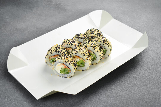 Japanese sushi roll set with sesame seeds served in white paper takeaway tray. Tasty rolls filled with cream cheese and cucumber. Fresh seafood.