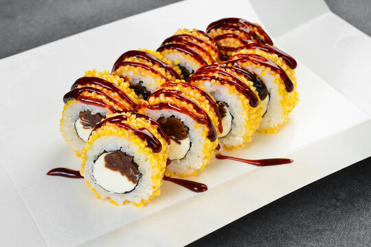 Crispy sushi rolls topped with sweet unagi sauce served in white takeaway paper tray. Gourmet Japanese rolls filled with cream cheese. Tasty seafood meal.