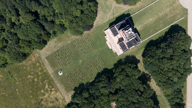 Aerial view of Thiepval Memorial to the Missing of the Somme surrounded by manicured lawns, rows of grave markers, and dense woodland in Thiepval, Hauts-de-France, France.
