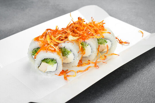 Japanese sushi rolls topped with crunchy fried onion and spicy sauce served in white takeaway paper box. Fresh rolls filled with cream cheese. Tasty food.