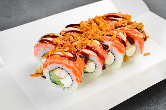 apanese salmon sushi roll set topped with crispy fried onions and sweet unagi sauce on white background. Tasty rolls filled with cream cheese. Fresh food.