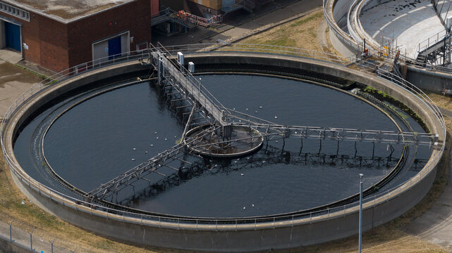 Aerial view of the M Group Water treatment facility featuring a large circular sedimentation tank with a rotating bridge mechanism in Dartford, England, United Kingdom.