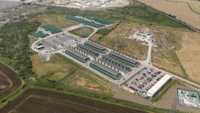 Aerial view of the Thurrock Flexible Generation Substation with rows of power generators, green containers, and a parking lot surrounded by fields, Tilbury, England, United Kingdom.