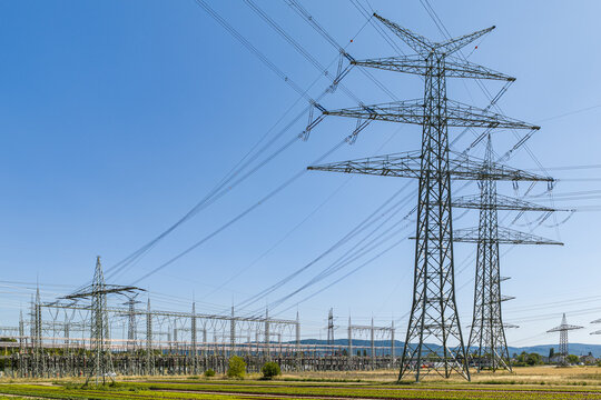 Aerial view of the Amprion-Umspannwerk electrical substation featuring large high-voltage transmission towers and power lines set against a clear blue sky in Pfungstadt, Hessen, Germany.