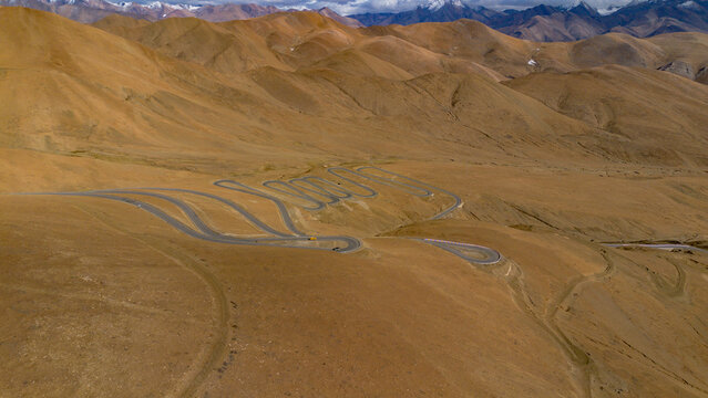 Aerial view of the winding serpentine road at Gawula pass surrounded by arid mountain slopes and distant snow-capped peaks in Shigatse, Tibet, China.