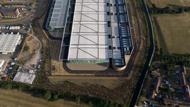Aerial view of a large modern industrial warehouse facility with a white roof, green facade, and surrounding paved roads in Waltham Cross, England, United Kingdom.