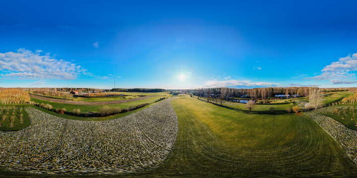 Aerial view of a golf course covered in early morning frost with patches of green grass and surrounding trees under a clear blue sky in Valmiera, Valmiera, Latvija.