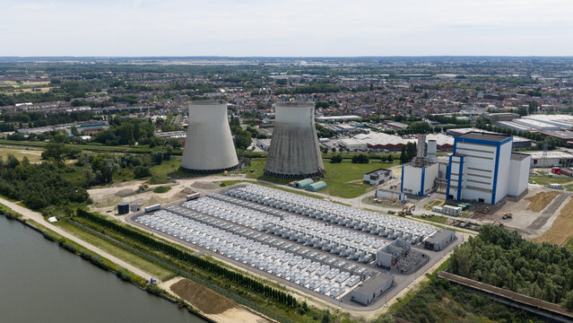 Aerial view of the Vilvoorde power plant with two cooling towers, a large battery energy storage system, and industrial buildings next to a canal in Vilvoorde, Flanders, Belgium.