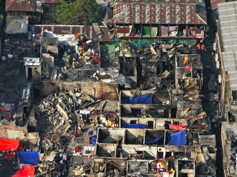 Aerial view of the fire-damaged Korail Basti settlement with charred structures, debris, and people navigating the ruins in Dhaka, Dhaka Division, Bangladesh.