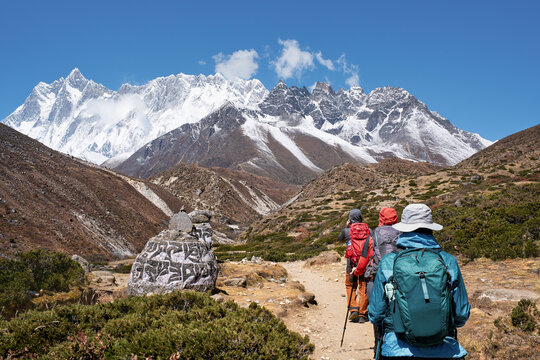 Hikers trekking on Everest Base Camp trail walking past sacred Mani prayer stone against majestic Himalayan mountains background, Nepal