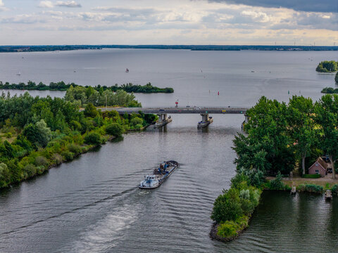 Aerial view of a barge navigating the waterway near Harderhaven, with a bridge, lush green trees, and the expansive Wolderwijd lake in Zeewolde, Flevoland, Netherlands.