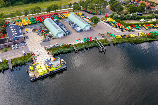 Aerial view of Rijkswaterstaat Harderhaven facility featuring rows of colorful navigation buoys, storage warehouses, and a work vessel docked at the pier in Zeewolde, Flevoland, Netherlands.
