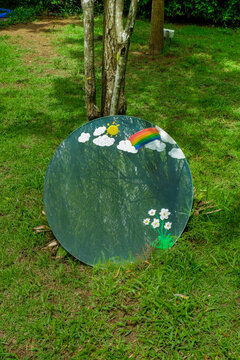 Round mirror with reflection on green grass in forest and big tree,metal round reflecting soft natural light with greenery in park,backyard,fantasy concept,space for text.