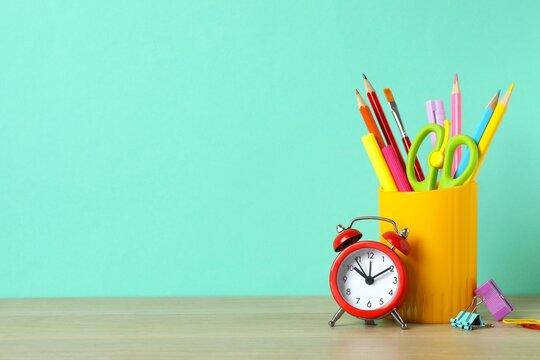 Holder with stationery and red alarm clock on wooden table