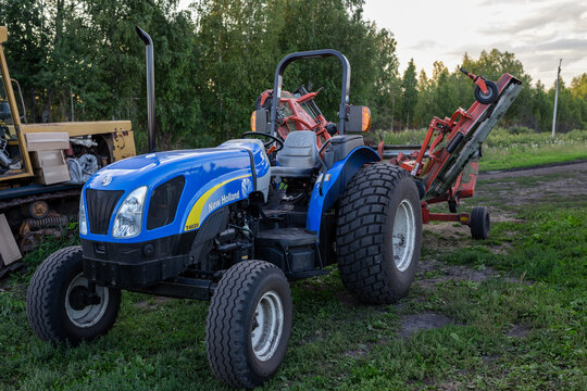TYUMEN, RUSSIA - AUGUST 15, 2013: blue tractor with harvesting equipment attached stands on green field