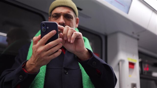 Mature man commuting on public transport checking his mobile phone, scrolling on social media, using an app on his smartphone, or reading messages on the subway train