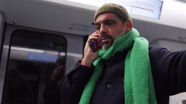 Stylish man talking on his smartphone while traveling on a subway train, showcasing modern urban commuting and constant connectivity in public transportation