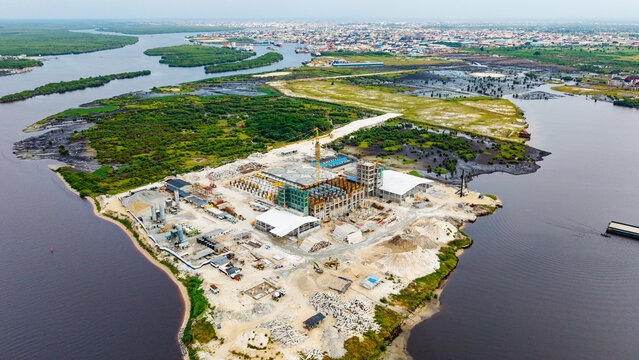 Aerial view of a construction site in Satellite Town with industrial buildings, a crane, and material stockpiles on a peninsula in the Lagos Lagoon, Lagos, Lagos, Nigeria.