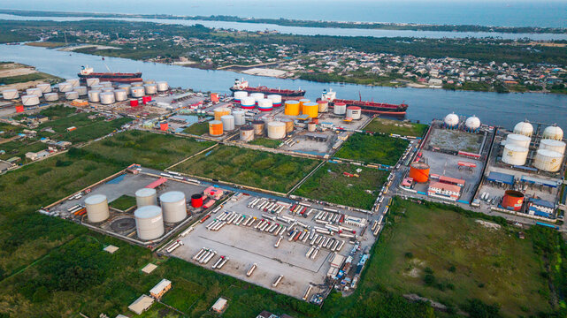 Aerial view of the industrial tank farm and shipping terminal in Satellite Town, featuring large storage tanks, cargo ships, and a parking lot filled with tanker trucks in Lagos, Lagos, Nigeria.
