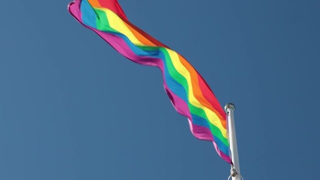 Stockholm, Sweden A Pride flag flies on a flagpole against a blue sky. 
