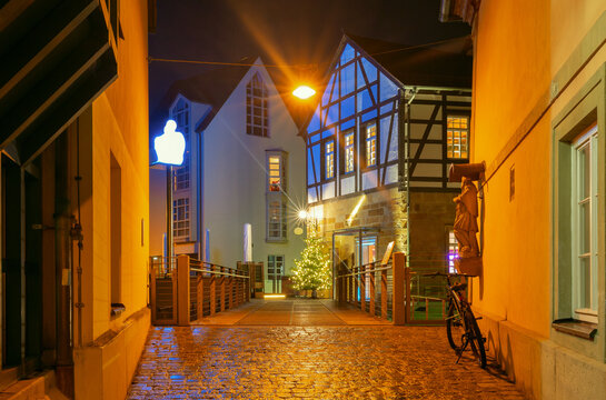 Night view of traditional half-timbered buildings, illuminated streets and a decorated Christmas tree in the historic center of Bamberg, Bavaria, Germany.