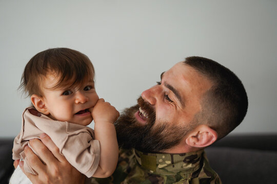 Military soldier wearing uniform while holding baby son at home - Emotional homecoming, love and family concept