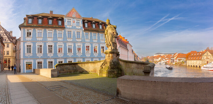 Historic bridge statue overlooking the Regnitz River with traditional waterfront architecture in the old town of Bamberg, Bavaria, Germany.