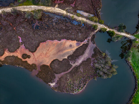 Aerial view of Point Fraser featuring unique reddish-brown marshland, dark water channels, and a winding dirt path along the riverbank in East Perth, Western Australia, Australia.