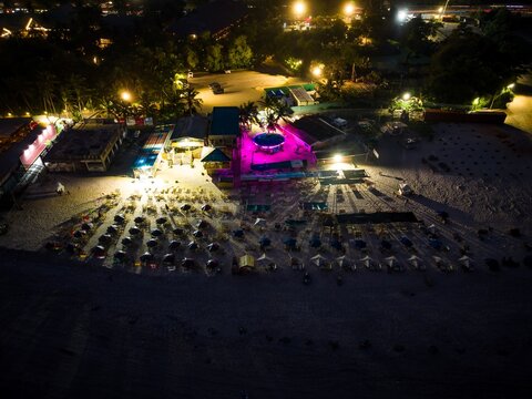 Aerial view of a beach resort at night with illuminated structures, rows of umbrellas on the sand, and vibrant purple lighting in Ghana.