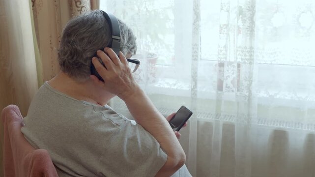 Senior Woman Nodding to Music While Using Smartphone Near Window