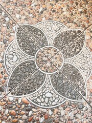 Obraz premium Top-down view of square stone tiles featuring an intricate, geometric medallion or floral pattern made of multi-colored pebbles, dark gray stones, and white gravel set in concrete.