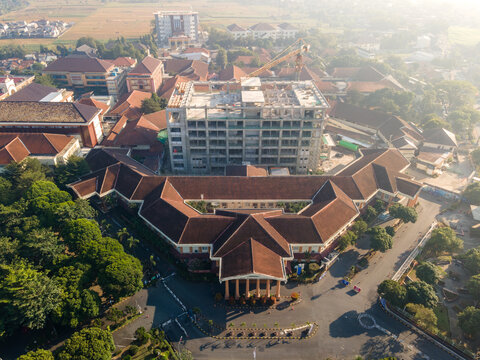 Aerial view of an institutional building complex with red-tiled roofs and a central courtyard, featuring a concrete structure under construction in Banyumas Regency, Central Java, Indonesia.