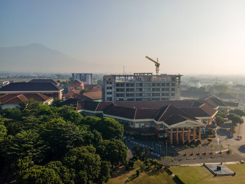 Aerial view of a building complex under construction with a crane, surrounded by lush trees and a distant mountain in Banyumas Regency, Central Java, Indonesia.