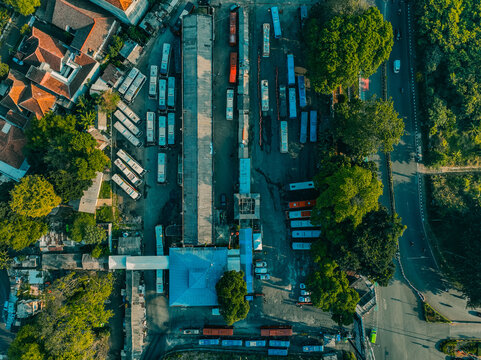 Aerial view of Baranangsiang bus terminal with rows of parked buses, a terminal building with a blue roof, and surrounding lush trees in Bogor Timur, West Java, Indonesia.