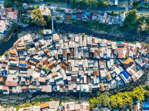 Aerial view of the dense residential neighborhood of Baranangsiang with closely packed rooftops and a river flowing through the urban landscape in Bogor Timur, West Java, Indonesia.