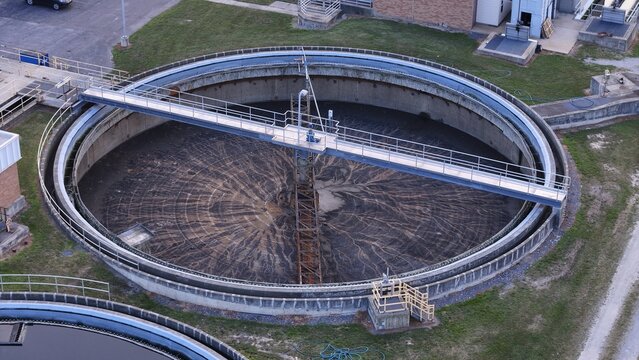 Aerial view of a circular water treatment facility with a large sedimentation tank, metal bridge walkway, and industrial infrastructure in Monroe, Michigan, United States.
