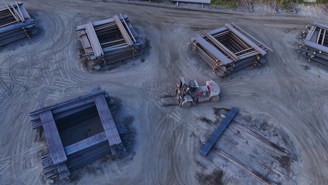 Aerial view of stacks of steel ingots arranged in a yard with a forklift operating on the dirt ground in Monroe, Michigan, United States.