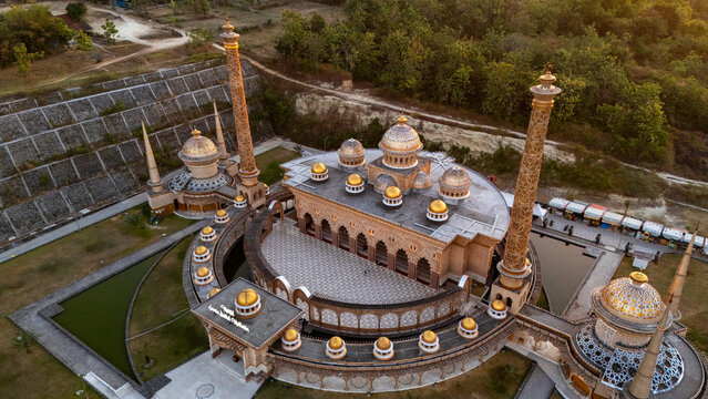 Aerial view of the ornate mosque with golden domes and tall minarets surrounded by lush greenery and a pond in Bojonegoro, East Java, Indonesia.