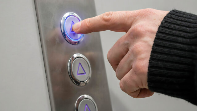 Human hand pushing an illuminated elevator call button with elevator technology building indicator navigation interior