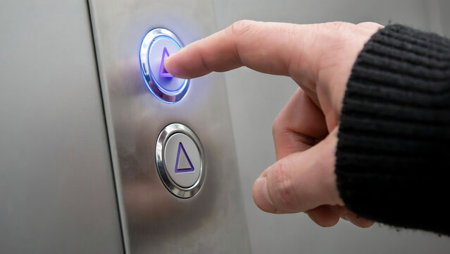 Person pressing an illuminated elevator control button to call the lift with elevator technology building indicator navigation interior