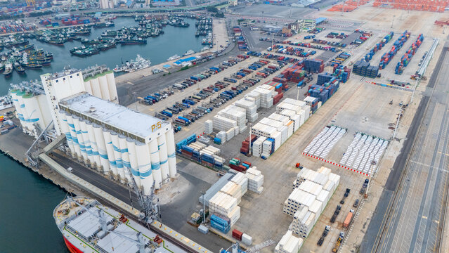 Aerial view of Busan Port featuring large grain silos, rows of shipping containers, and cargo ships docked at the industrial waterfront in Busan, Busan, South Korea.