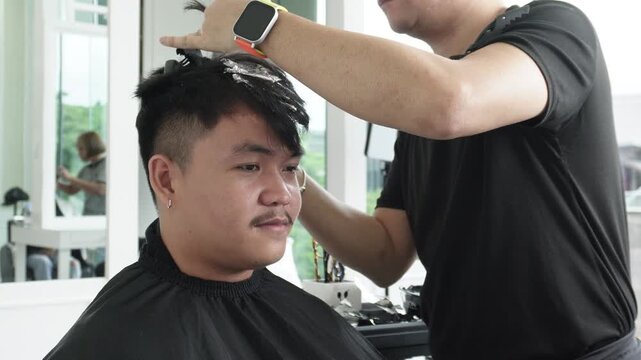 Hair stylist sectioning hair and placing foils for highlights during professional hair highlighting treatment for an Southeast Asian man in his early 20s