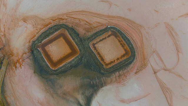 Aerial view of Koyuncu Salt Works, showing two distinct square salt evaporation ponds with reddish-brown water surrounded by textured salt flats in Sereflikochisar, Ankara, Turkiye.