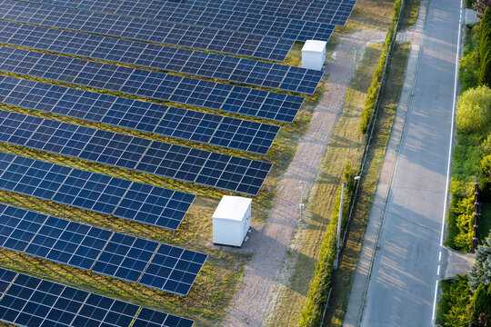 Aerial view of a large solar farm with rows of photovoltaic panels, white electrical cabinets, and a paved road nearby in Krakow, Lesser Poland Voivode, Poland.