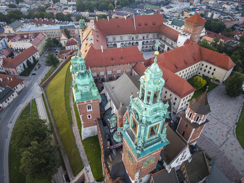 Aerial view of Wawel Royal Castle featuring its historic red tile roofs and ornate green copper cathedral domes surrounded by city streets and greenery in Krakow, Malopolskie, Poland.