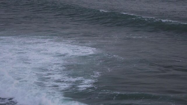 Large waves rolled in the middle of the sea, with white foam visible. Elevated view